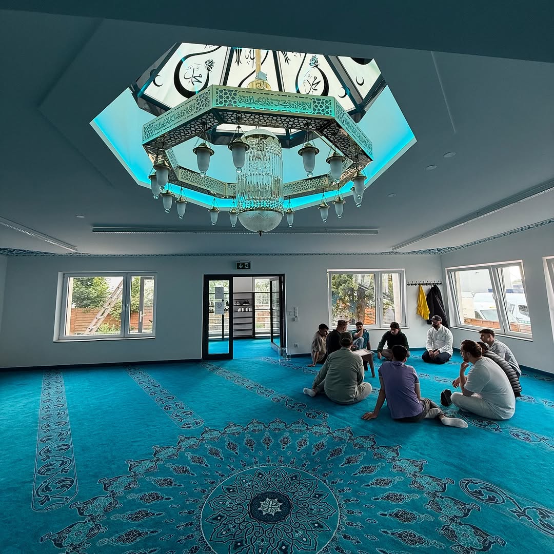 Gebetsraum der Moschee mit türkisfarbenem Teppich und Kronleuchter